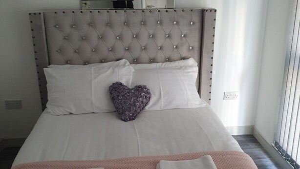 A neatly made bed with a heart-shaped pillow, a pink blanket, and two folded towels. - Immaculate 3-bed Studio in Liverpool City Centre (Liverpool)