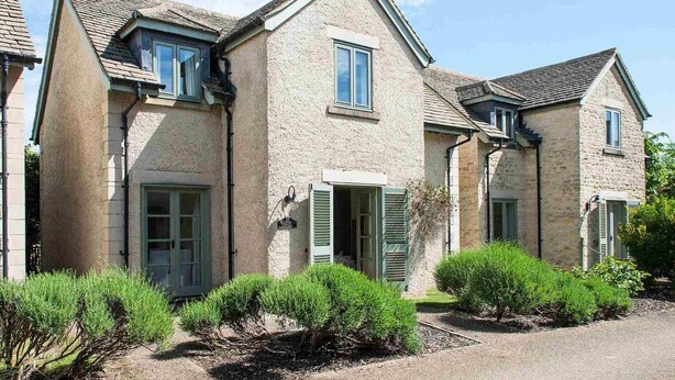 A two-story stone house with a gravel driveway and green shrubs. - Mill Village 59, Millstream Cottage (P) - On-site Facilities, Pool, Sleeps 6 (Somerford Keynes)