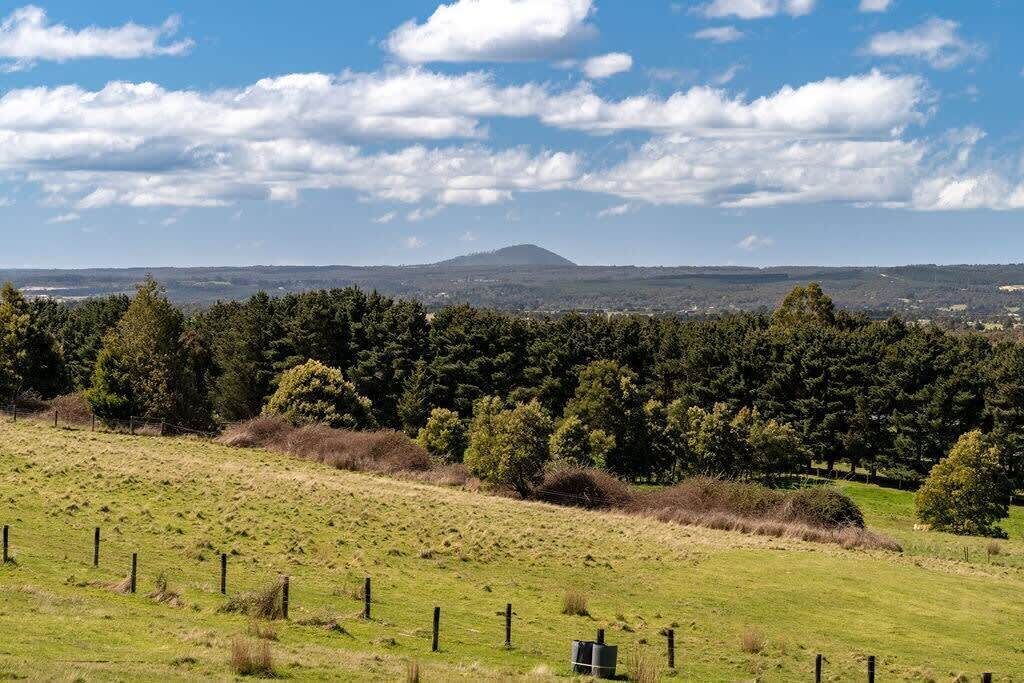 Paisagem rural com um campo cercado, árvores e uma colina ao longe.