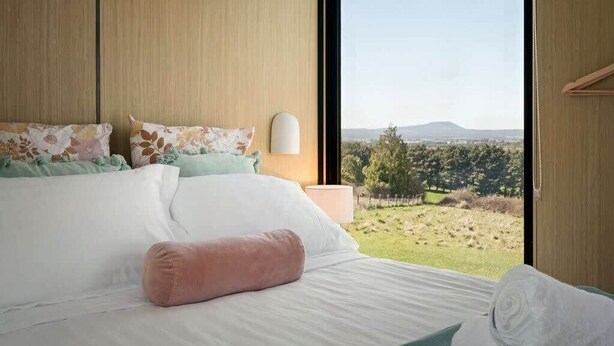 Un dormitorio con un ventanal grande, una cama con ropa de cama blanca y vistas a un paisaje.