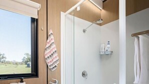 Un baño moderno con ducha de vidrio, un lavamanos con espejo y una ventana con vistas al exterior.