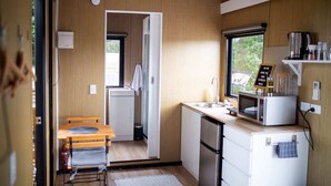 A compact kitchen with a microwave, sink, and a small dining area with a bench. - Pacific View by Tiny Away (Leithfield)