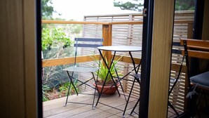 A wooden deck with a metal table and chairs, a potted plant, and a view of greenery. - Pacific View by Tiny Away (Leithfield)