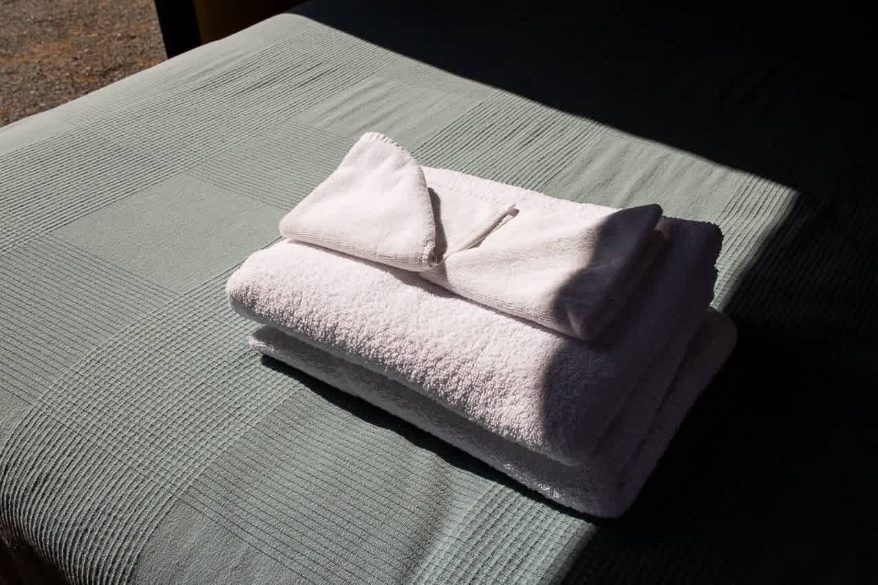 Een keurig opgevouwen witte handdoek op een gestructureerd grijs bed.