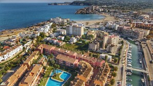 Zona costera con complejo turístico, piscina, edificios frente a la playa y puerto deportivo.