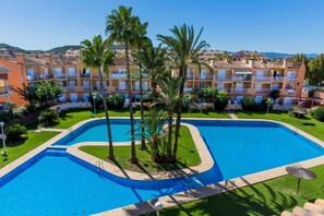 A swimming pool with a curved design, surrounded by palm trees and a well-maintained lawn. - Arenal Park II Apartment Javea Arenal, with Terraces, AC and common areas with large Swimming Pool, Garden, Tennis, Paddle (Javea / Xàbia)