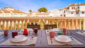 Mesa de comedor dispuesta con platos, vasos y cubiertos, con vistas a una hilera de edificios con tejados de teja.