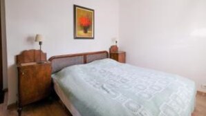 Un dormitorio con una cama, una mesita de noche de madera, una lámpara y un cuadro en la pared.