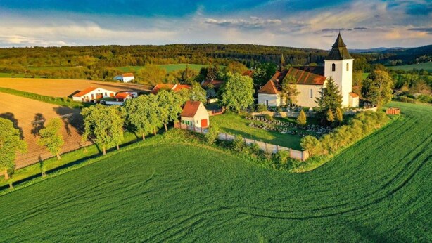 Un pueblo rural con una iglesia destacada, rodeado de campos y pequeñas casas.