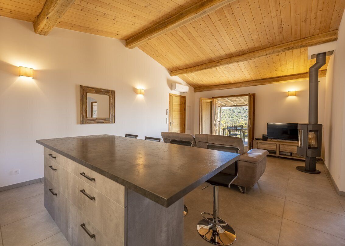 A spacious living area with a large island, wooden ceiling beams, a television, and a fireplace.