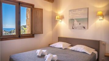 A bedroom with a bed, two bedside lamps, a painting, and a window with a view.