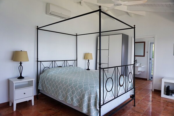 Una cama con dosel con una colcha estampada, dos mesitas de noche con lámparas, un tocador blanco y un armario blanco con espejo.