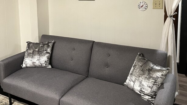 A grey sofa with metallic cushions, a patterned rug, and a wall with three paintings depicting ocean scenes.