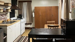 A compact kitchen with white cabinets, a stove, and a wooden dining table with chairs.