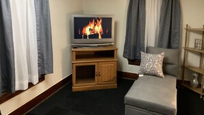 A living room with a television displaying a fireplace, a grey sofa, and wooden furniture.