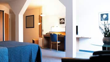Quarto de hotel com cama, escrivaninha, cadeira, abajur e quadro na parede.