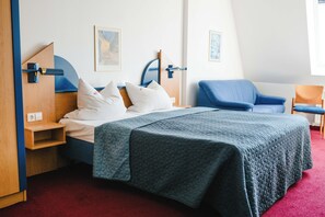 Un dormitorio con una cama, una silla azul, una mesita de noche de madera y una alfombra roja.