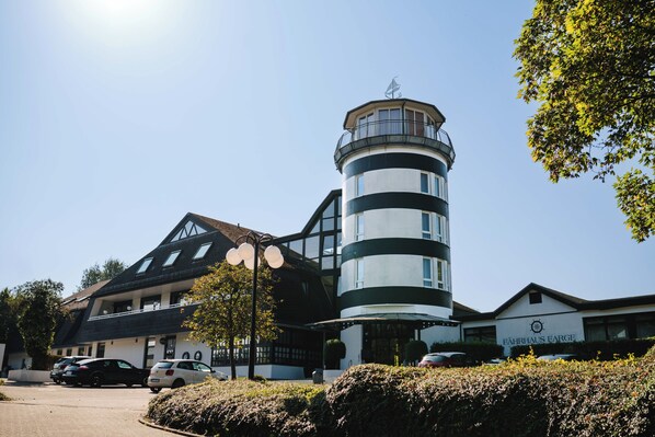 Un edificio con una torre cilíndrica, un cartel que dice "FAHRHAUS FARGE" y un estacionamiento con coches.