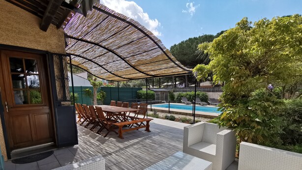 Eine Terrasse mit Holztisch und -stühlen, einem Pool und einer überdachten Sitzgelegenheit.