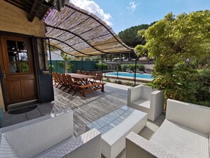 Un patio con mesa y sillas de madera, una piscina y un área de estar cubierta.