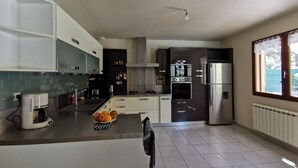 Eine moderne Küche mit weißen Schränken, einer zentralen Kochinsel mit Obst, einem Einbauofen und einem Kühlschrank.