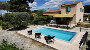 Ein Schwimmbecken mit Liegestühlen, eine überdachte Terrasse und ein Haus mit einem Ziegeldach.