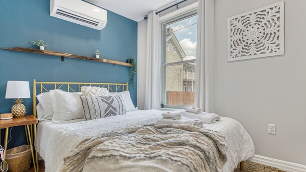 A bedroom with a bed, a bedside table with a lamp, a window with a view, and a decorative wall piece. - Cozy, dog-friendly, downtown (Frederick)