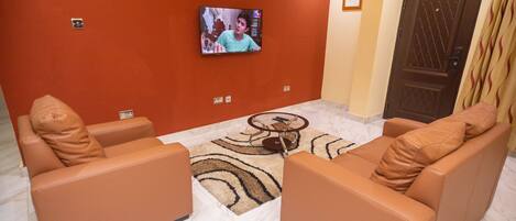 Una sala de estar con dos sofás de cuero marrón, una mesa de centro, un televisor montado en la pared, un tapete estampado y una puerta con un diseño decorativo.