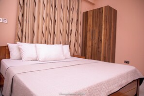 Ein ordentlich bezogenes Bett mit weißen Leinen und Kissen, ein Holzschrank und ein wellenförmiger Vorhang.