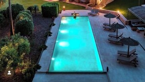 Une grande maison à deux étages avec une piscine, entourée d’une végétation luxuriante et avec des collines en arrière-plan.