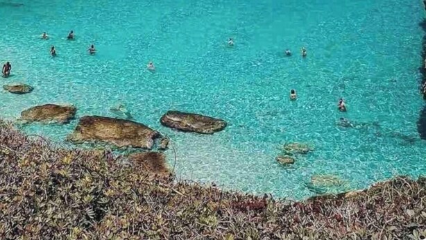 Un paysage côtier avec une eau turquoise et limpide, des falaises rocheuses et un bateau.