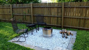 Un patio trasero con un brasero, dos sillas de metal y una mesa.