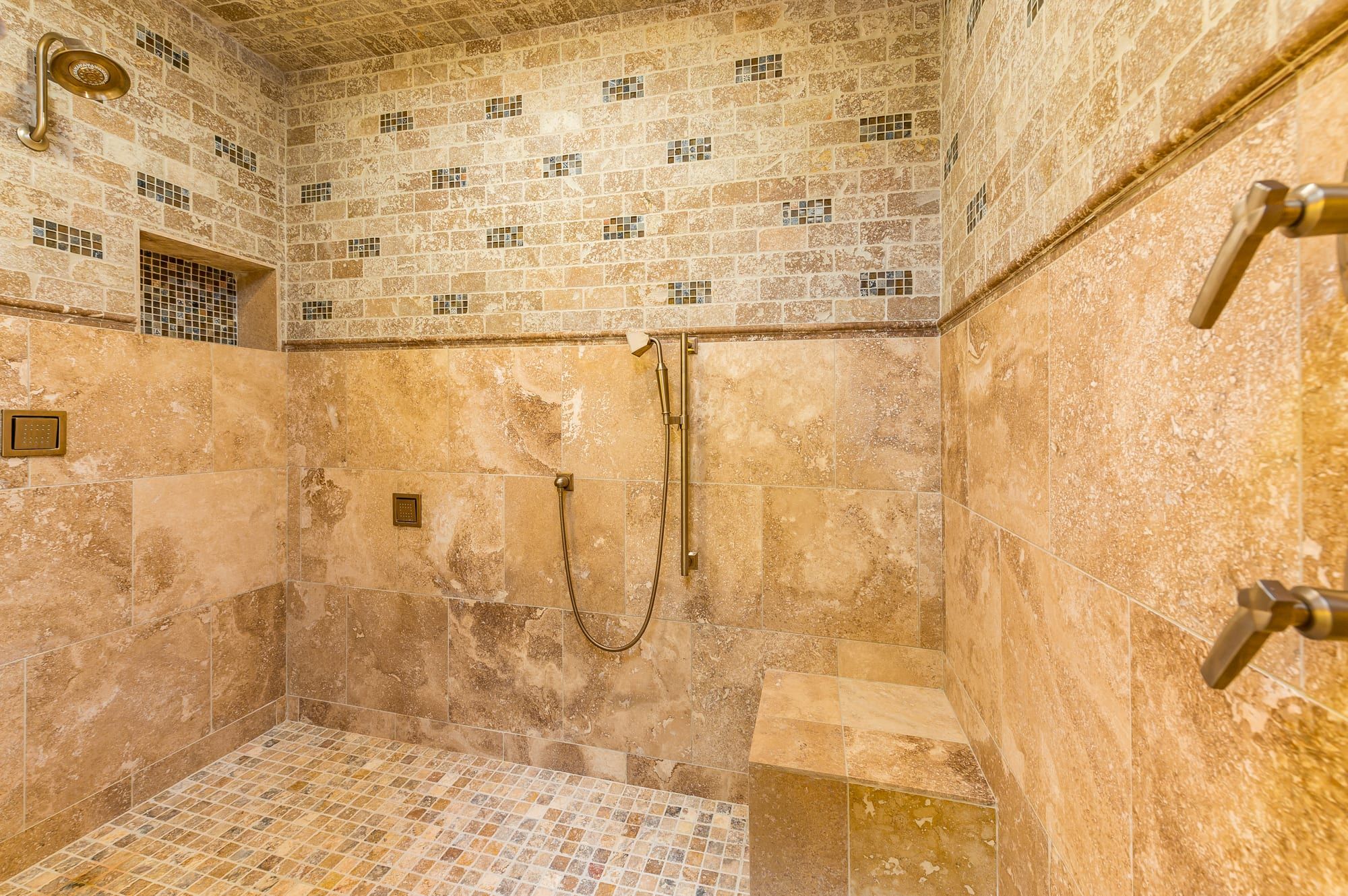 Une salle de bain avec un sol carrelé, un espace douche et un mur orné d’une mosaïque.