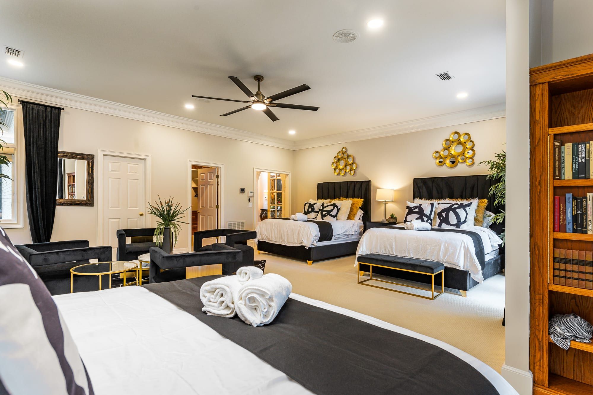 A hotel room with two beds, a ceiling fan, a bookshelf, and a large mirror.