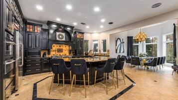 A modern kitchen with dark cabinetry, a central island, and a dining area with black chairs and a chandelier.