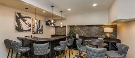 A modern bar area with a curved counter, bar stools, and pendant lighting.