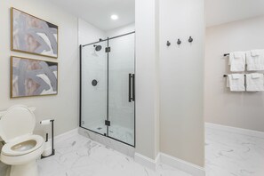 A modern bathroom with a glass-enclosed shower, a toilet, and two framed abstract paintings on the wall. - Abbey Manor on Pinehurst #6- Golf Views -Sleeps 24 (Pinehurst)