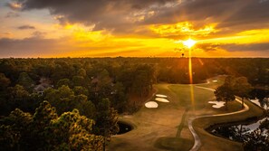 A golf course with a sunset view, surrounded by dense forest and a few buildings. - Abbey Manor on Pinehurst #6- Golf Views -Sleeps 24 (Pinehurst)