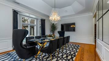 A dining area with a long table, black chairs, a chandelier, and a patterned rug.