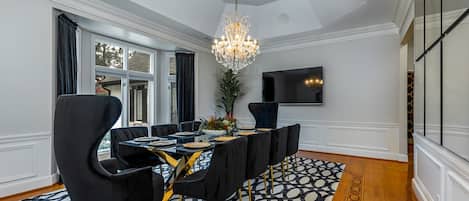 A dining area with a long table, black chairs, a chandelier, and a patterned rug.