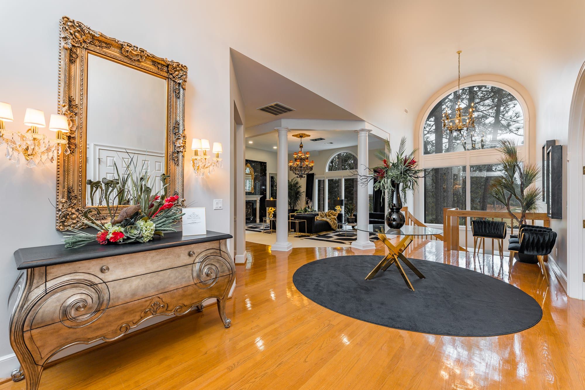 A spacious living room with a large ornate mirror, a black round rug, and a dining area with a wooden table and chairs.