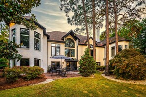 A multi-story house with a patio area featuring outdoor furniture. - Abbey Manor on Pinehurst #6- Golf Views -Sleeps 24 (Pinehurst)