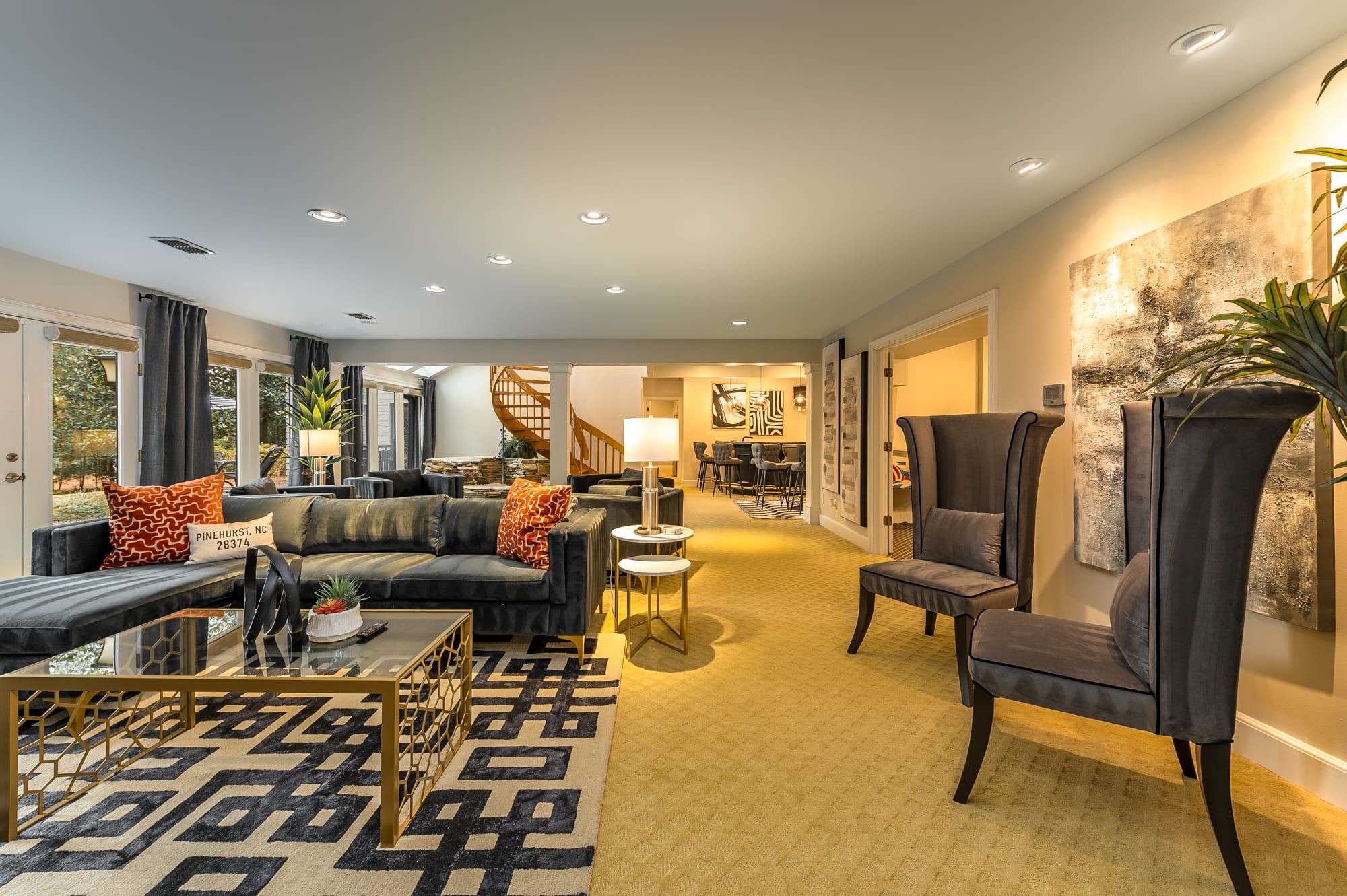 A modern living room with a sofa, armchairs, and a coffee table. There is a staircase leading to another level, and a dining area in the background.