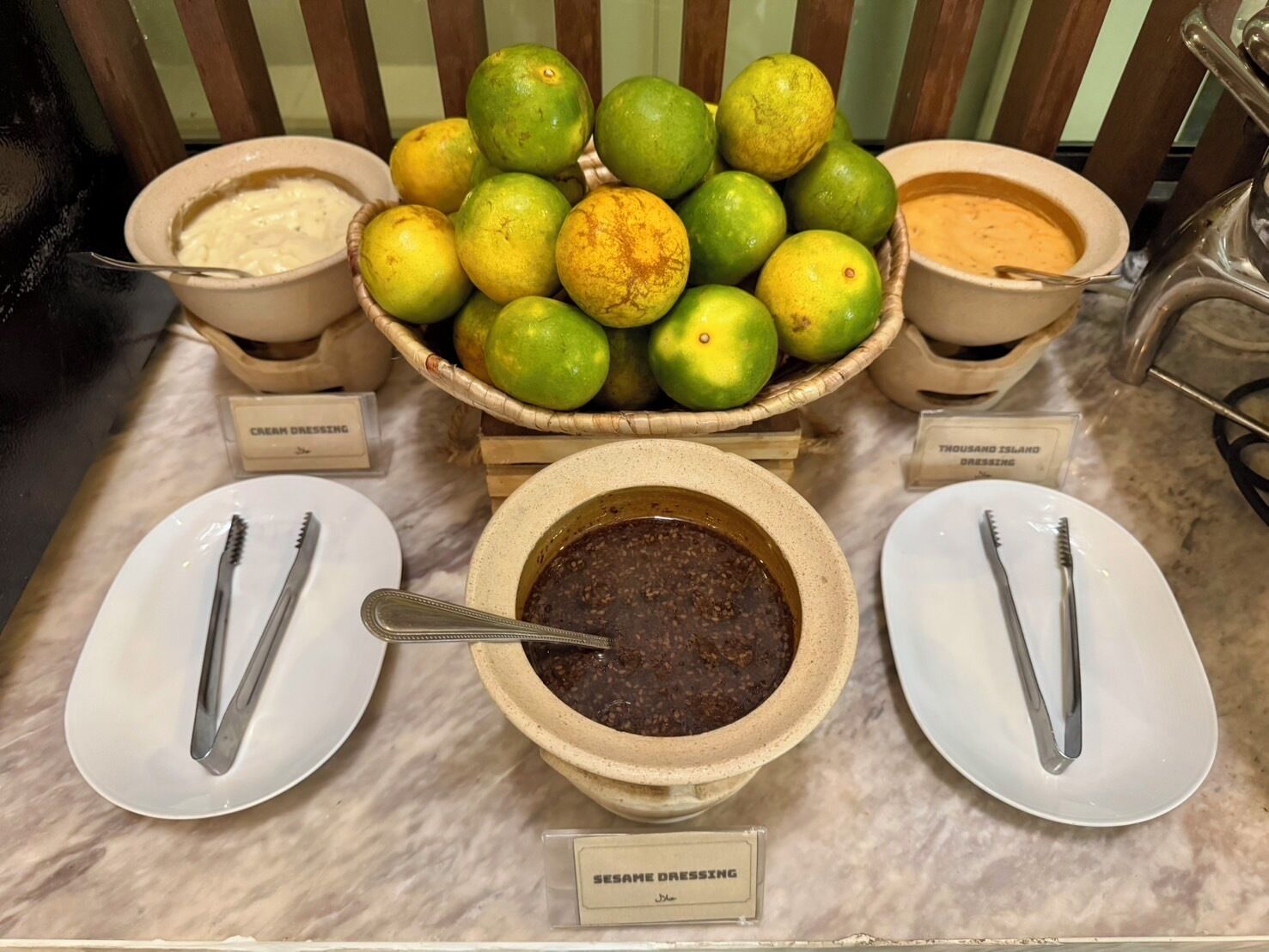 A buffet table with bowls of cream dressing, Thousand Island dressing, and sesame dressing, along with a bowl of green limes.