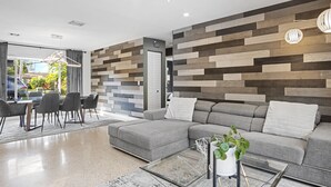 A modern living room with a sectional sofa, a glass coffee table, and a wooden wall panel. - Beach Bliss: Heated Pool, BBQ & Tropical Vibes 🌊 (Oakland Park)