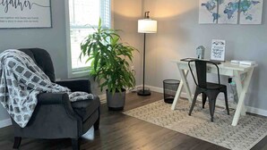A modern living room with a grey armchair, a potted plant, a desk with a chair, and a world map artwork on the wall.