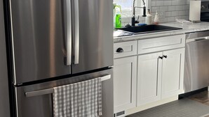 A modern kitchen with stainless steel appliances, white cabinetry, and a black countertop.