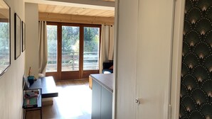 Ein Flur, der zu einem Balkon führt, mit Holzboden, einem Tisch mit Büchern und einer Tür mit ornamentalem Wandpapier.