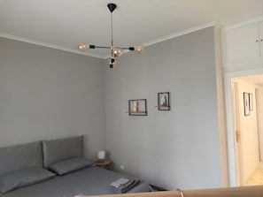 Un dormitorio con cama, mesita de noche, lámpara y luz empotrada en la pared.