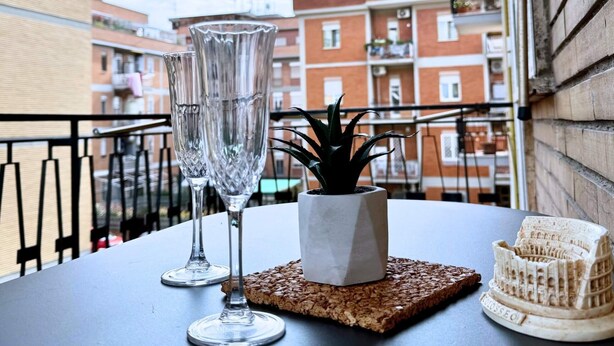 Un balcón con dos vasos transparentes, una pequeña planta en maceta y una réplica en miniatura del Coliseo sobre un posavasos.